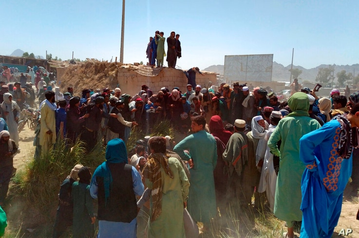 Taliban fighters and Afghans gather around the body of a member of the security forces who was killed, inside the city of Farah…