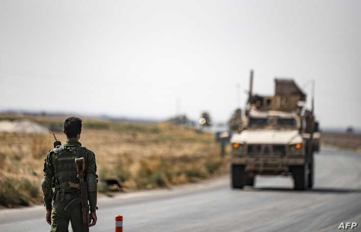 A fighter from the Syrian Democratic Forces SDF stands guard as a convoy of US military vehicles drives on a road after US…