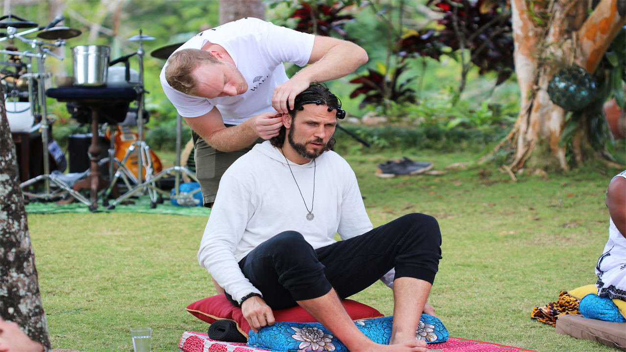 A photo of a Riley Cote sitting on a mat outside while someone attached a device to his head.