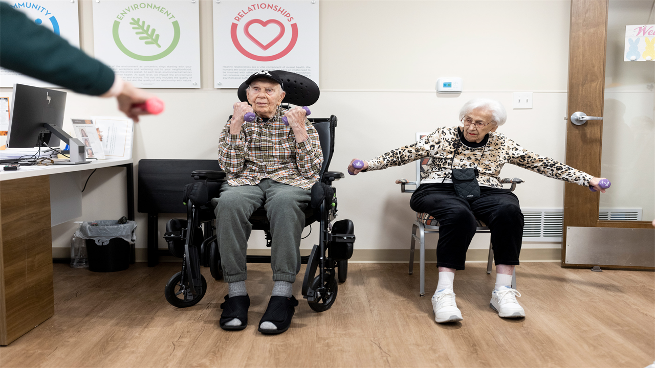 A photo of an elderly couple using small dumbbells to exercise while seated.