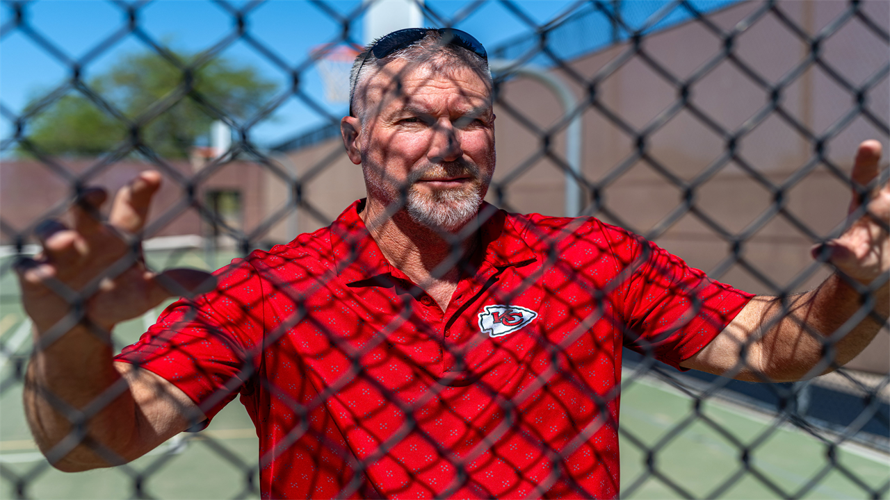 A photo of Bradley Little posing for a portrait behind a wire fence.