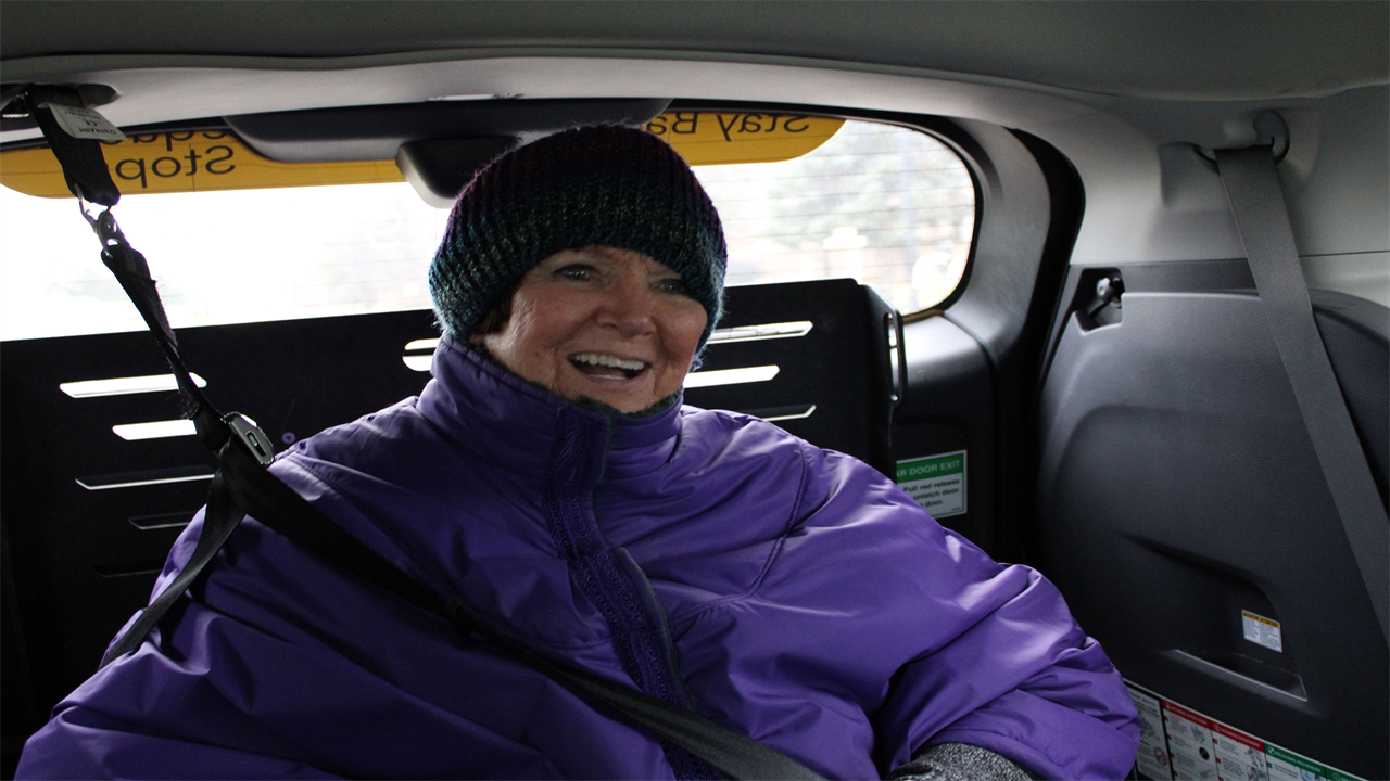 A portrait of Myrna Peterson. She is sitting in an electric wheelchair which is secured in the back of the goMARTI van.
