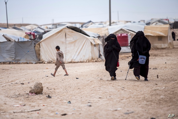 Women walk in the al-Hol camp that houses some 60,000 refugees, including families and supporters of the Islamic State group,…