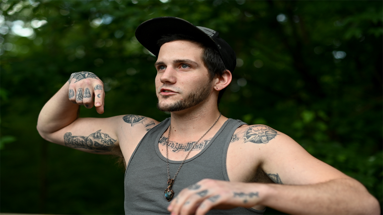 By motioning with his arms, Adam Caprioli describes being shot in the back with a pepper-spray launcher while having a mental health crisis.