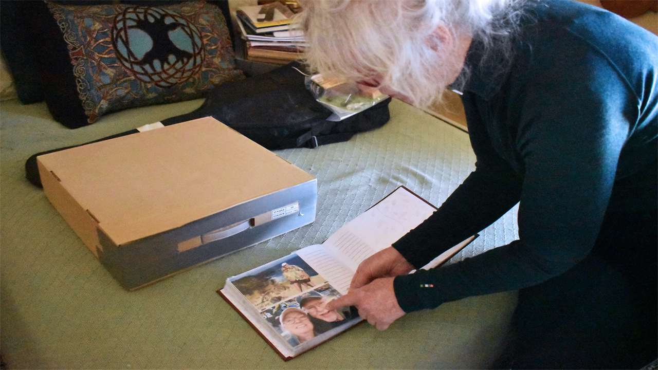 A photo shows a woman pointing to a photo of her husband in a photo book.