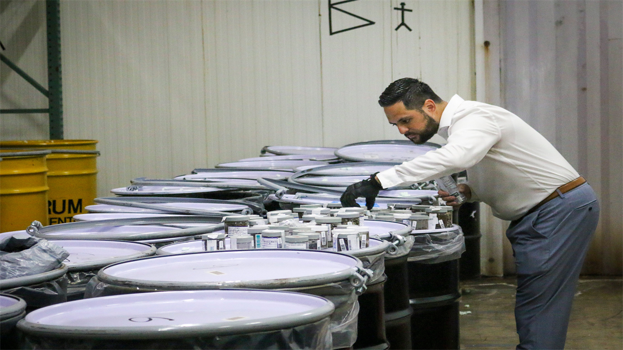 A photo shows a man wearing protective gloves examining the contents of a jar inside a storage facility.