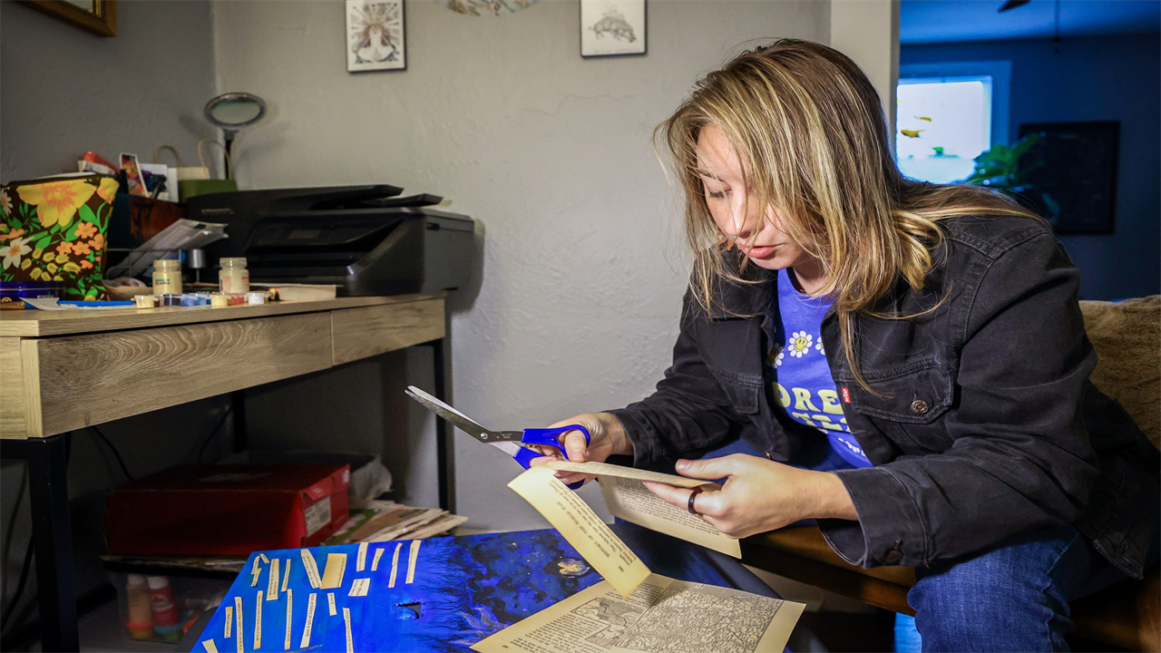Nina Shand works on her art at home in St. Petersburg, Florida. She is cutting up pages from an old book, picking out words and sentence fragments.