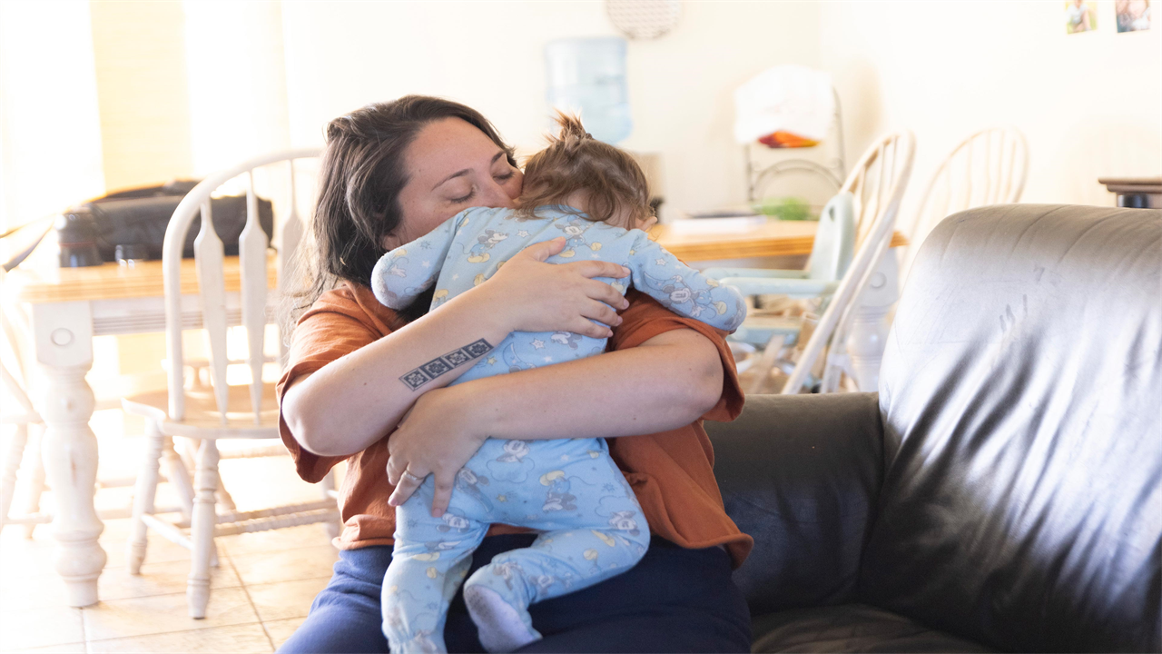 A photo of a mother hugging her infant son while sitting on the couch.